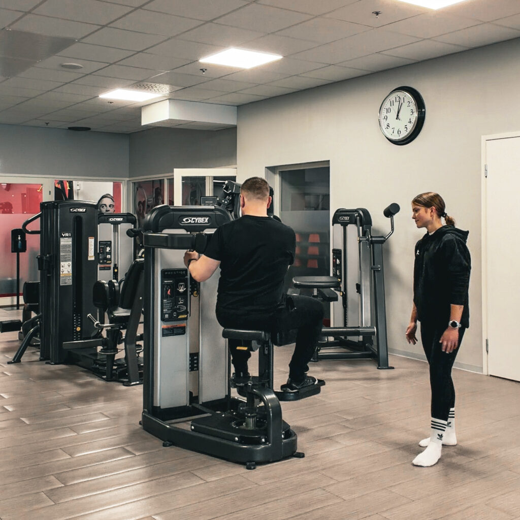 Valmentaja tarkistaa liikeradan Fit Lahti kuntosalilla.
