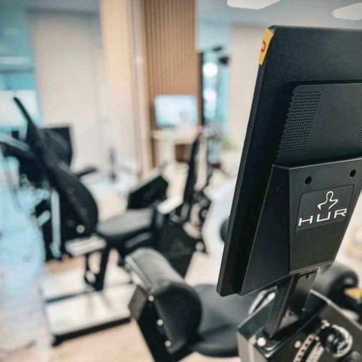 HUR-älykuntosalin harjoituslaitteen näyttö ja taustakuvaa salilta.